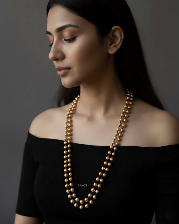 Woman wearing a long gold dholki necklace against a dark background